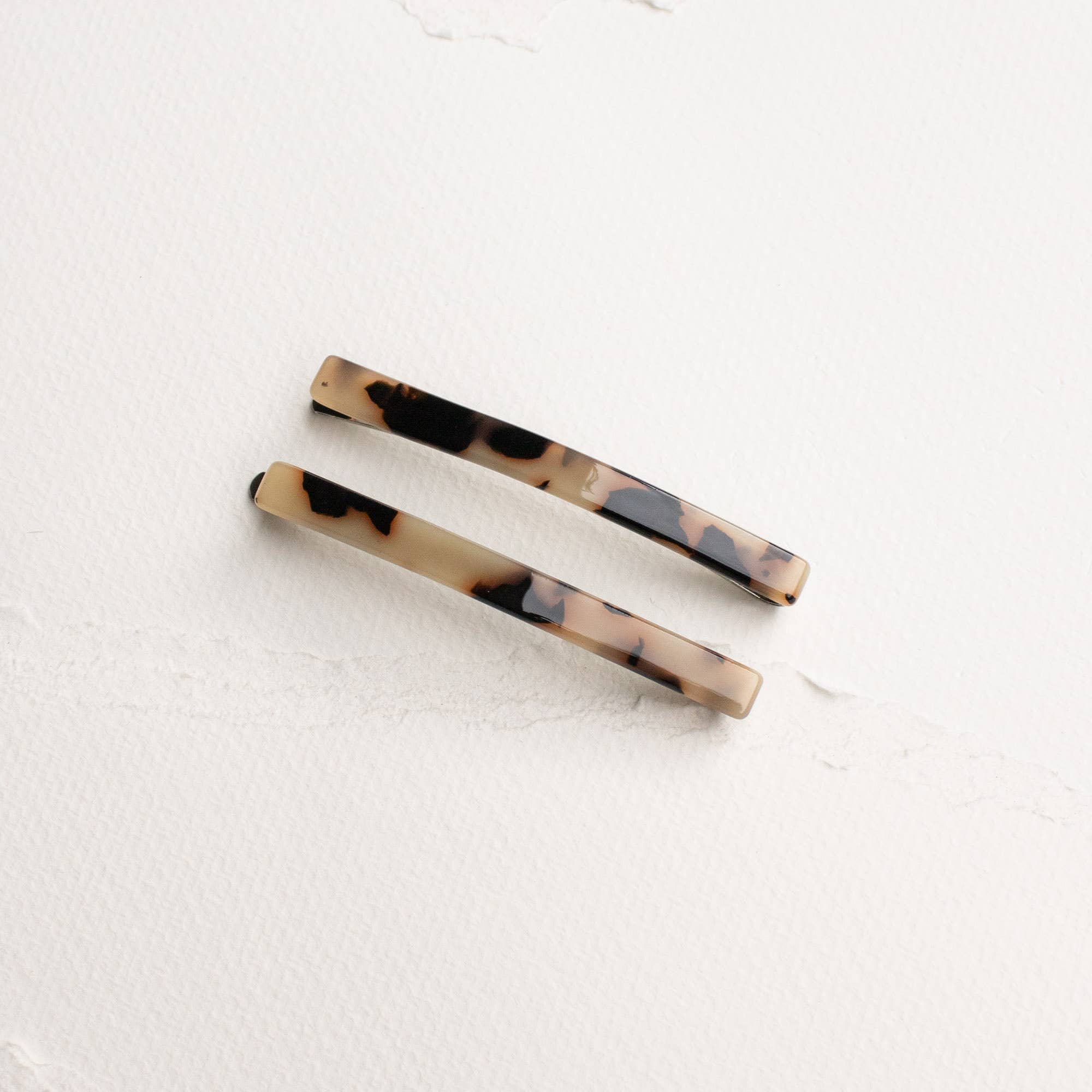 Two tortoiseshell barrettes on a white textured background