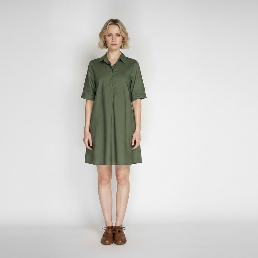 A woman modeling a short-sleeve olive green shirt dress with a buttoned collar, standing against a light gray studio background.
