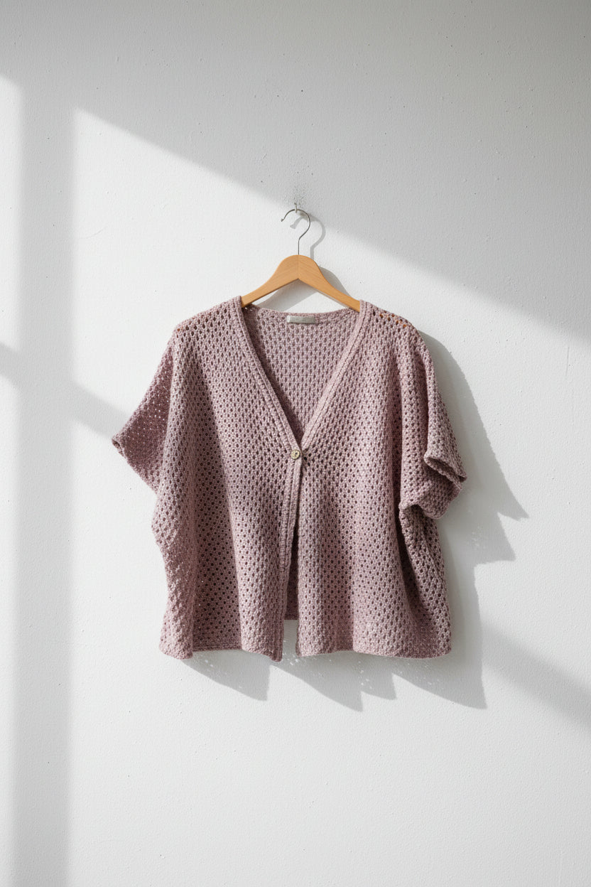 Pink crochet top on a hanger against a white background