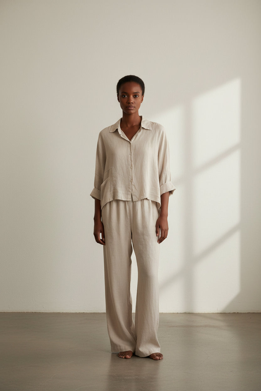 Woman wearing a beige linen shirt and pants in a bright room with natural light.