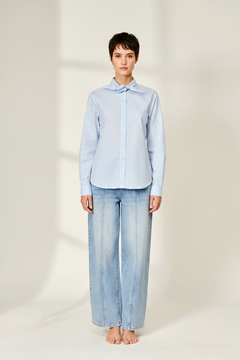 Woman wearing a light blue striped shirt and jeans on a beige background