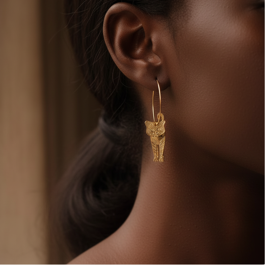 Close-up of a gold hoop earring with a small animal charm worn by a person.
